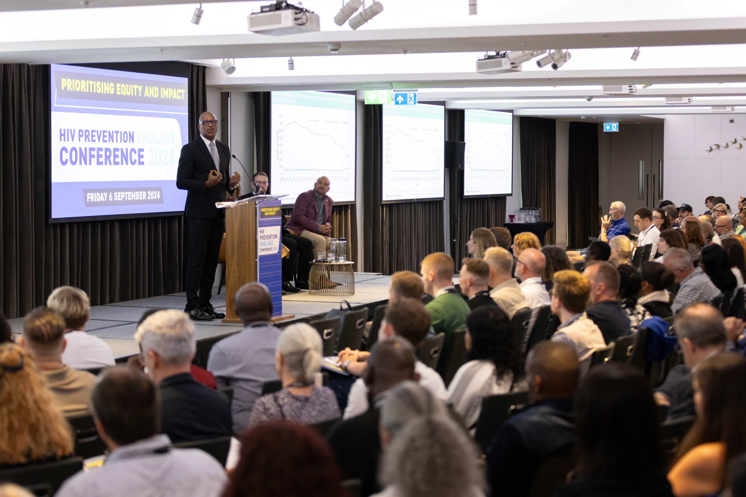 Kevin Fenton addresses a large conference. Behind him is a slide which reads HIV Prevention England 2024.